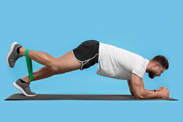 Young man exercising with elastic resistance band on light blue background