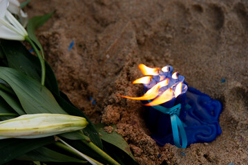 Blue candles with a lit flame and a white flower on the beach sand. Gift for Iemanja the queen of...