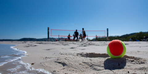 Doubles beach tennis game on the beach with blue sky and beach tennis ball in the foreground.