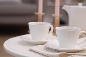 Cups of tea and teapot on white table indoors