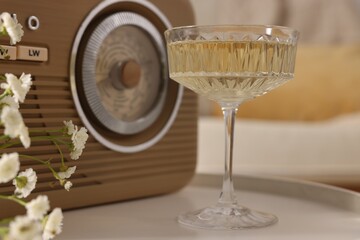 Glass of alcohol drink, flowers and radio set on table in room, closeup. Relax at home