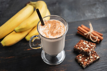 Glass of protein milkshake drink with straw and scoop of whey protein powder, protein bar and bananas on a dark wooden board, bodybuilding food supplements