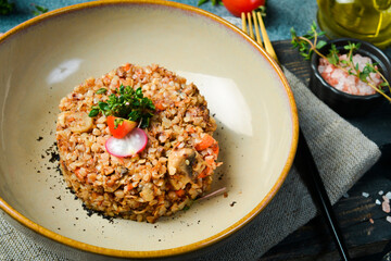 Boiled buckwheat with mushrooms and tomatoes. Healthy food. Dietary nutrition. On a dark stone background.