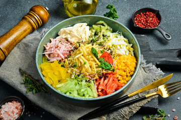 A plate of colorful vegetable salad made of cucumber, paprika, tomatoes, potatoes and boiled sausage. On a dark stone background.