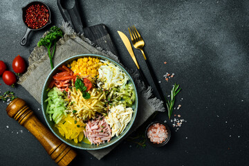 A plate of colorful vegetable salad made of cucumber, paprika, tomatoes, potatoes and boiled sausage. On a dark stone background.