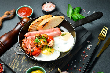 Traditional American breakfast: fried eggs, sausage, bacon and vegetables in a frying pan. Homemade food. On a dark stone background.