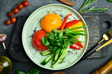 Cutting fresh vegetables: tomatoes, paprika, parsley, cilantro, onions. On a plate. On a dark stone background.