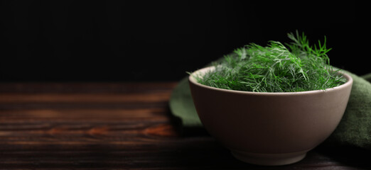Fresh dill in bowl on wooden table against black background. Banner design with space for text