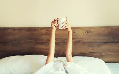 Cheerful lazy woman waking up after sleeping lying in soft comfortable bed showing empty cup coffee...