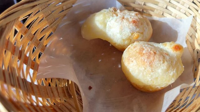 Typical brazilian cheese buns in a paper bag over wooden table. take cheese buns with tongs from a knitted wicker basket from a white napkin operative delicious food bun three things together