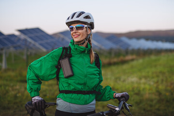 Portrait of a beautiful cyclist standing in front of solar panels at a solar farm.
