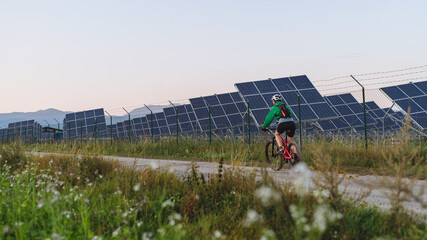 Rear view of a female cyclist riding in front of solar panels at a solar farm.