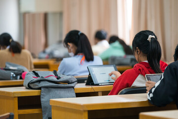 University students concentrate on doing examinations via tablet and smartphone in the classroom
