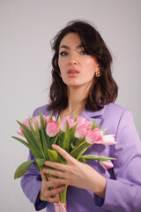 Beautiful brunette woman in violet costume with bucket of tulips, flowers, sitting on high chair. Girl smile, happy. Portrait of young office manage. Smile and freshness