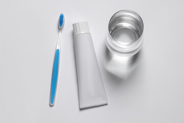 Plastic toothbrush with paste and glass of water on white background, top view