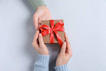 Man giving gift box to woman on light gray background, top view