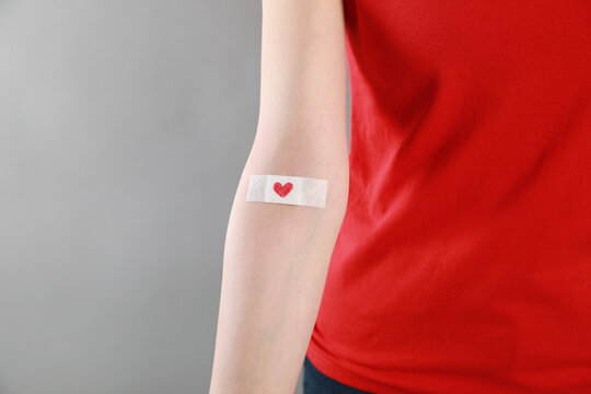 Blood donation concept. Woman with adhesive plaster on arm against grey background, closeup. Space for text