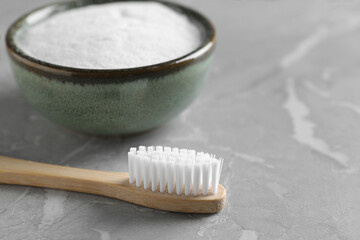 Bamboo toothbrush and bowl of baking soda on light gray marble table, closeup