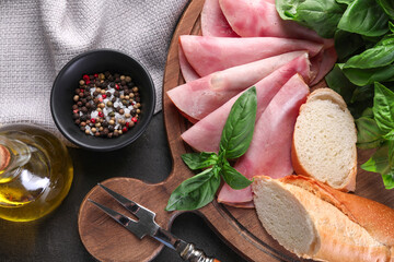 Tasty ham with basil, bread, spices and carving fork on table, flat lay