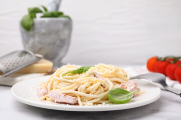 Plate of tasty pasta Carbonara with basil leaves on white marble table, closeup
