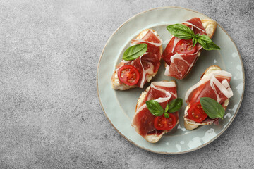 Tasty sandwiches with cured ham, basil and tomatoes on grey table, top view. Space for text