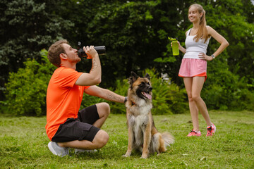 Naklejka na ściany i meble Couple drinking water while spending time with their dog in park