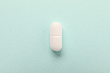 One white pill on mint background, top view