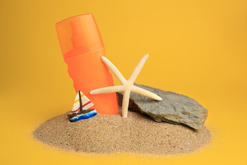 Sand with bottle of sunscreen, starfish, stone and ship figure against orange background. Sun protection