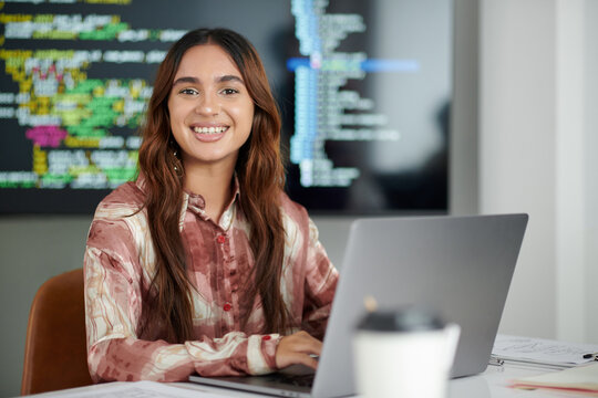 Portrait of joyful young software developer working on laptop in modern office