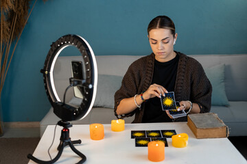 Fortune teller woman reading future on tarot cards recording video for her blog. Ritual candles...