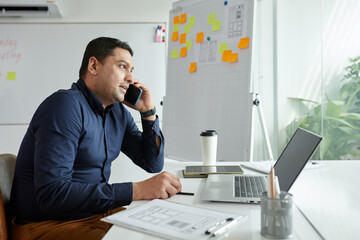 Fototapeta premium Entrepreneur sitting at office desk and talking on phone with client