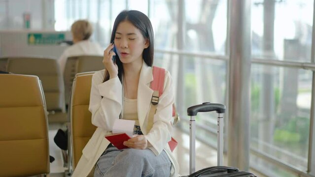 Smiling young asian woman sitting in waiting room and talking over smartphone with friend or family. Beautiful female traveller talking on cell phone at airport lounge. Woman on phone.