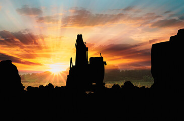 Obraz premium Crawler excavators silhouette are digging the soil in the construction site. on sunset background