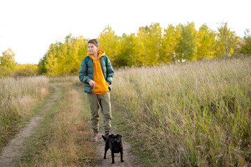 Fototapeta premium Teen boy with a dog walking in the park on a sunny yellow autumn. Friendship of boy and animal, animal owner. Portrait of boy with pet.