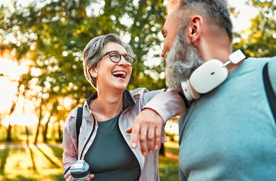 Smiling beautiful stylish cheerful sincere carefree happy gray-haired senior woman in glasses and sportswear rests hand on friend and laughs while talking outdoors.Morning run.