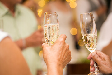 A group of people cheering with champagne glasses at a wedding. The focus is on the hands and glasses. The people are all smiling and looking happy.