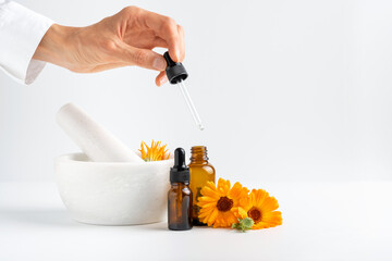 Calendula flowers in mortar, amber glass bottles with essential oil and pharmacist hand with...