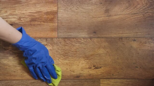 Woman's hand in blue glove wipes floor with rag.