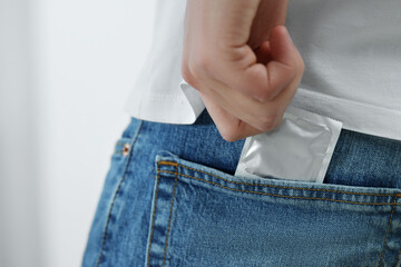 Man pulling condom out of pocket on blurred background, closeup. Space for text