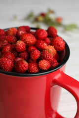 Fresh wild strawberries in mug on white table, closeup