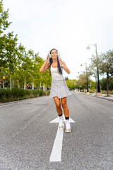 Beautiful woman is listening to music, skating at the street, smiling and looking forward