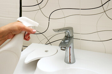 female hand spraying cleaning agent on sink and faucet in bathroom