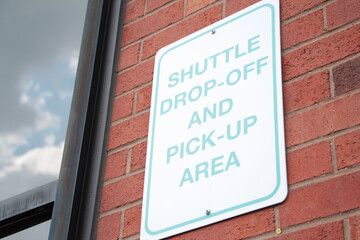shuttle drop off and pick up area rectangle vertical sign on red brick wall next to window, white...