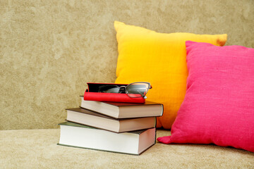 books with glasses with a case on a sofa with colorful pillows