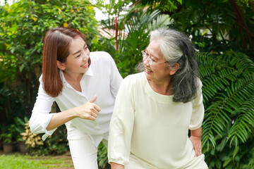 A caregiver or nurse does physical therapy for an elderly person in an outdoor garden. Daughter and...