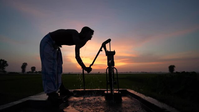 Silhouette of a person using a hand pump, tube well to draw fresh water during a mesmerizing sunset. This evocative video captures the beauty of daily life in rural India.