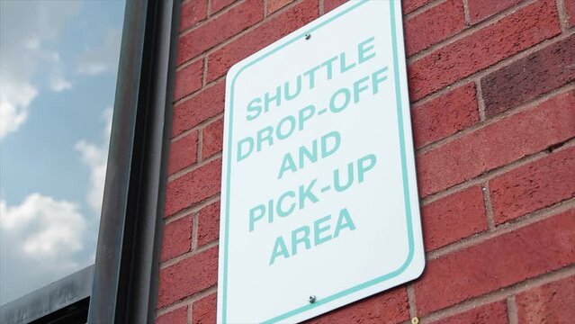 shuttle drop off and pick up area rectangle vertical sign on red brick wall next to window, white and blue, close up