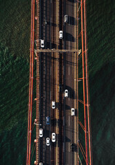 Vertical photo of traffic on bridge crossing the river - top view. Bridge in Lisbon (Portugal) with cars and other vehicles from above (aerial view). Traffic of the road (bridge) on sunset time.