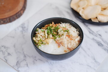 Rice porridge with chicken in black bowl on white marble table