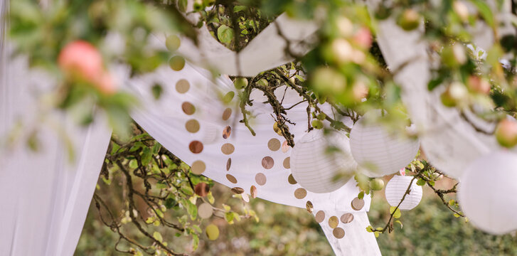 viele wei&szlig;e Lampions, Papierlaternen, Glitzerkette und wei&szlig;es Tuch dekorativ, festlich h&auml;ngen im Apfelbaum. F&uuml;r Festival, Party, Hochzeit
